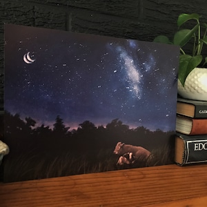 Pode incluir: Uma impressão que retrata uma cena noturna com uma lua crescente e um céu estrelado. Duas vacas estão em um campo de grama alta. A obra de arte tem uma paleta de cores escuras e sombrias com tons de azul, roxo e marrom.