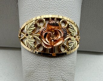 May include: A gold ring with a rose design. The rose is made of three different colors of gold: yellow, white, and rose. The ring is set with a delicate filigree design.