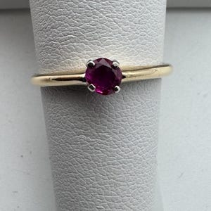 May include: A gold ring with a single round ruby gemstone.
