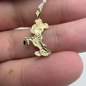 K&ouml;nnte beinhalten: Ein kleiner, goldfarbener Anh&auml;nger in Form einer Zeichentrickmaus, befestigt an einem d&uuml;nnen wei&szlig;en Faden. Der Anh&auml;nger weist aufwendige Details auf und scheint aus Metall zu bestehen. Die Maus befindet sich in einer Laufpose.