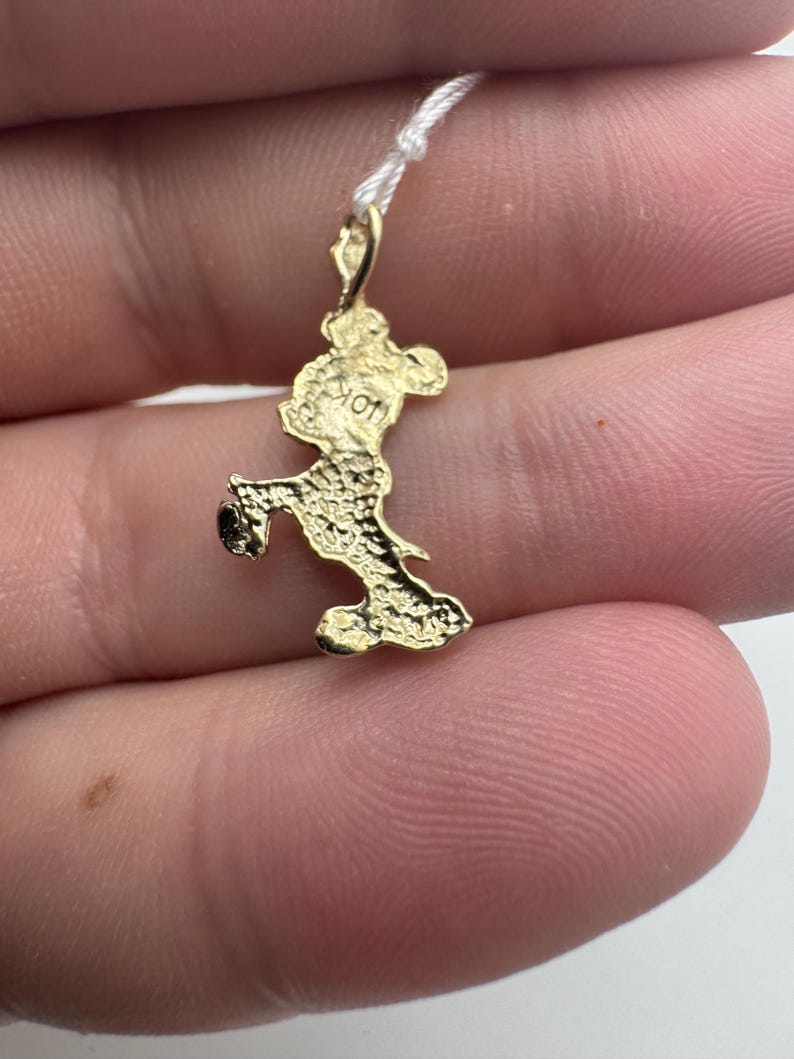 K&ouml;nnte beinhalten: Ein kleiner, goldfarbener Anh&auml;nger in Form einer Zeichentrickmaus, befestigt an einem d&uuml;nnen wei&szlig;en Faden. Der Anh&auml;nger weist aufwendige Details auf und scheint aus Metall zu bestehen. Die Maus befindet sich in einer Laufpose.