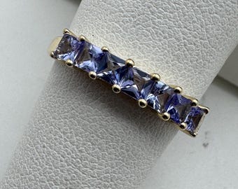 May include: A gold band ring with a row of six square-shaped purple gemstones.