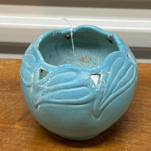 May include: A teal blue ceramic planter with a scalloped rim and leaf-shaped cutouts. The planter has a distressed finish and is perfect for displaying small plants or succulents.