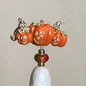 May include: A white ceramic Christmas tree with colorful light bulbs and a pumpkin topper. The topper features three orange pumpkins with carved faces and green stems.