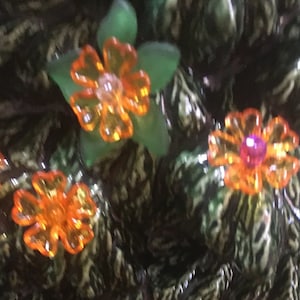 May include: A green ceramic Christmas tree with orange and pink flower-shaped ornaments. The tree is decorated with white lines and has a textured surface.
