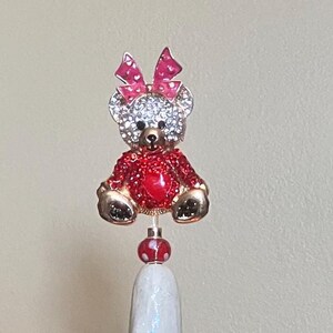 May include: A white ceramic Christmas tree with colorful lights and a jeweled bear topper. The tree has a textured surface and a white base.
