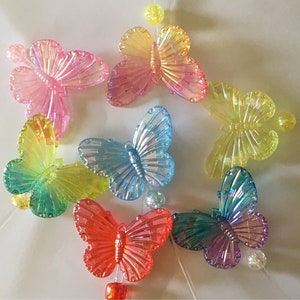 May include: Assortment of colorful iridescent butterfly charms made of plastic. The butterflies are in various shades of pink, blue, green, and purple.