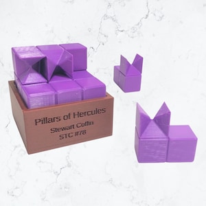 May include: A purple wooden puzzle box with the text "Pillars of Hercules Stewart Coffin STC #78" on the front. The puzzle box is open and shows a purple 3D puzzle inside. There are two additional purple 3D puzzle pieces on a white marble surface.
