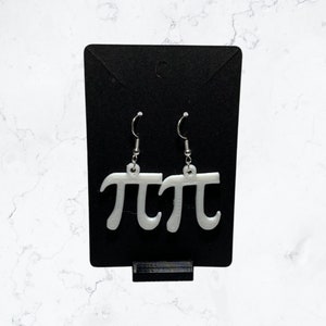 Puede incluir: Un par de pendientes de plata con símbolos pi impresos en 3D blancos.