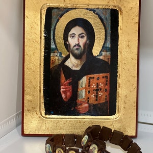 May include: A framed religious icon depicting Jesus Christ with a golden frame and a brown wooden background. The icon is surrounded by two brown wooden bracelets with small images of saints.