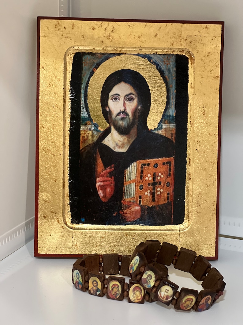 May include: A framed religious icon depicting Jesus Christ with a golden frame and a brown wooden background. The icon is surrounded by two brown wooden bracelets with small images of saints.