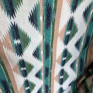 May include: A close-up of a woven fabric with a geometric pattern in shades of green, blue, and beige. The fabric has a textured surface and a slightly faded appearance.