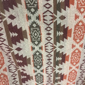 May include: Close-up of a textile with a repeating geometric pattern. The design features vertical stripes with alternating shapes in shades of brown, orange, and grey. The fabric has a slightly textured appearance, suggesting a woven material.
