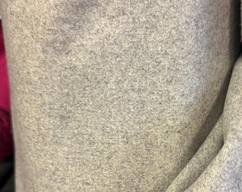 Puede incluir: Un rollo de tela gris claro con un aspecto texturizado y afelpado. El material está enrollado firmemente, con pliegues y sombras visibles que añaden profundidad. La tela parece suave y potencialmente adecuada para ropa o decoración del hogar.