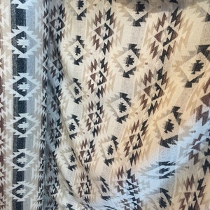 May include: White fabric with a brown, black and beige geometric pattern. The fabric has a woven texture and is folded in half.