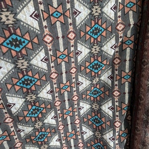 May include: A brown fabric with a repeating geometric pattern in shades of brown, white, blue, and orange. The pattern features triangles, diamonds, and stars.