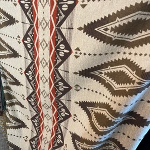 May include: A woven blanket featuring a geometric pattern in shades of brown, red, and white. The blanket has a traditional Native American design.
