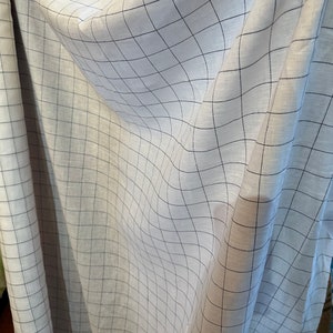 May include: White linen fabric with a black grid pattern. The fabric is folded and draped, showing the texture and weave of the material.