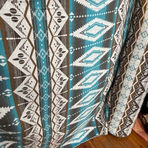 May include: A close-up of a turquoise, brown, and white patterned fabric with a geometric design. The fabric is folded and draped over a wooden surface.