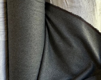 May include: A roll of dark gray fabric with a brown stripe along the edge. The fabric is folded and draped over a white surface.
