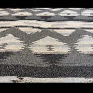 May include: A grey and white woven throw blanket with a geometric pattern.