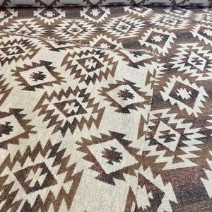 May include: A close-up of a woven fabric with a geometric pattern in shades of brown and white. The fabric has a textured surface and a repeating pattern of diamonds and triangles.