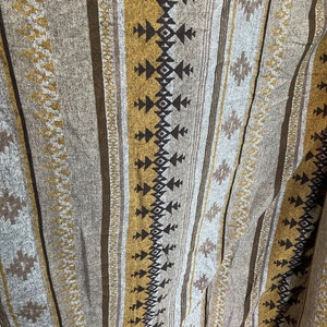 May include: A woven blanket with a striped pattern in shades of brown, beige, and gold. The blanket features a geometric design with black and white accents.