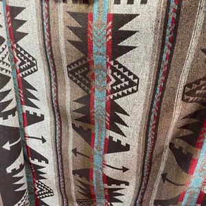 May include: A woven blanket with a geometric pattern in shades of brown, red, white, and blue. The pattern features triangles, arrows, and zigzags.