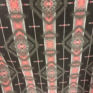 May include: Black fabric with a repeating pattern of pink, gray, and white geometric shapes. The pattern is reminiscent of Native American designs.