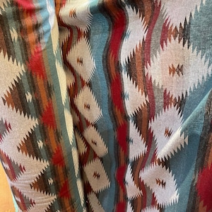 May include: A roll of fabric with a Southwestern-inspired pattern featuring geometric shapes in shades of red, brown, blue, and white.