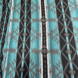 Peut inclure: Un gros plan sur un tissu tissé avec un motif répétitif de rayures turquoise, noires, grises et blanches. Le tissu a une surface texturée et un design traditionnel du sud-ouest.