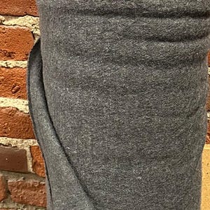 May include: A roll of dark grey fabric with a soft, fuzzy texture. The fabric is folded over itself and has a slight sheen.