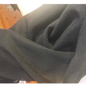 May include: Close-up of a dark fabric with a textured weave. The fabric appears to be a deep black colour, with subtle variations in tone and texture. The material is folded, creating shadows and highlights.