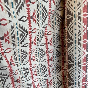 May include: Close-up of a fabric with a geometric pattern in shades of brown, red, and blue. The fabric has a woven texture and is folded in half.