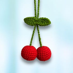 May include: Two red crocheted cherries with green crocheted leaves hanging from a string.
