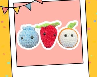 May include: Three crocheted plush toys shaped like a blueberry, strawberry, and orange. The blueberry is light blue, the strawberry is red, and the orange is white with orange accents. Each toy has black eyes and a simple smiling face.