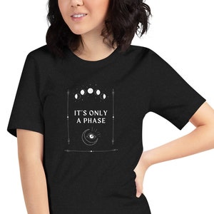 May include: Black t-shirt with a white graphic design featuring a crescent moon, an eye, and the text "It's only a phase".