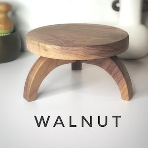 May include: A small, round wooden stand with three legs. The stand is made of walnut wood and has a natural finish. The stand is perfect for displaying small items, such as plants, candles, or jewelry.