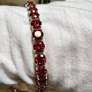 May include: A silver bracelet with a row of red round gemstones.