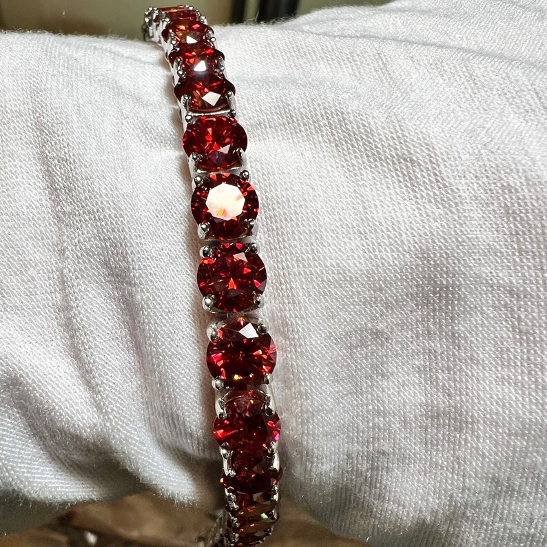 May include: A silver bracelet with a row of red round gemstones.