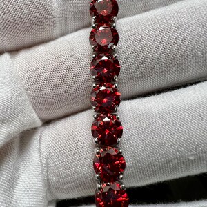 May include: A silver bracelet with a row of red round gemstones.