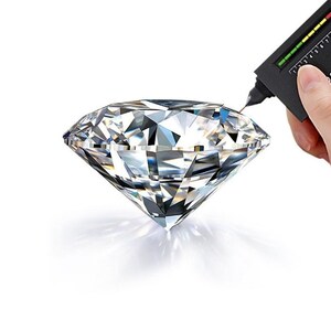 May include: A diamond is being tested with a diamond tester, a small handheld device with a scale and the words "SELECTOR II".