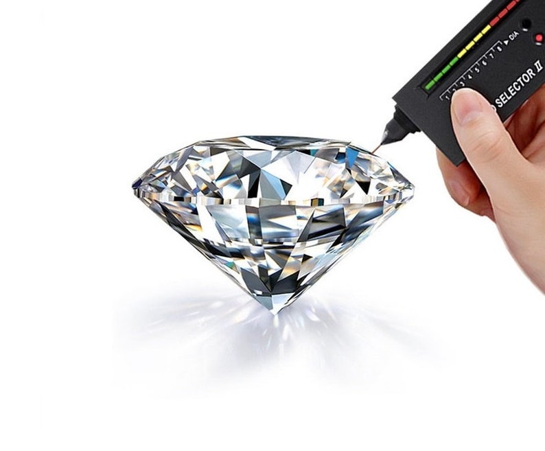 May include: A diamond is being tested with a diamond tester, a small handheld device with a scale and the words "SELECTOR II".