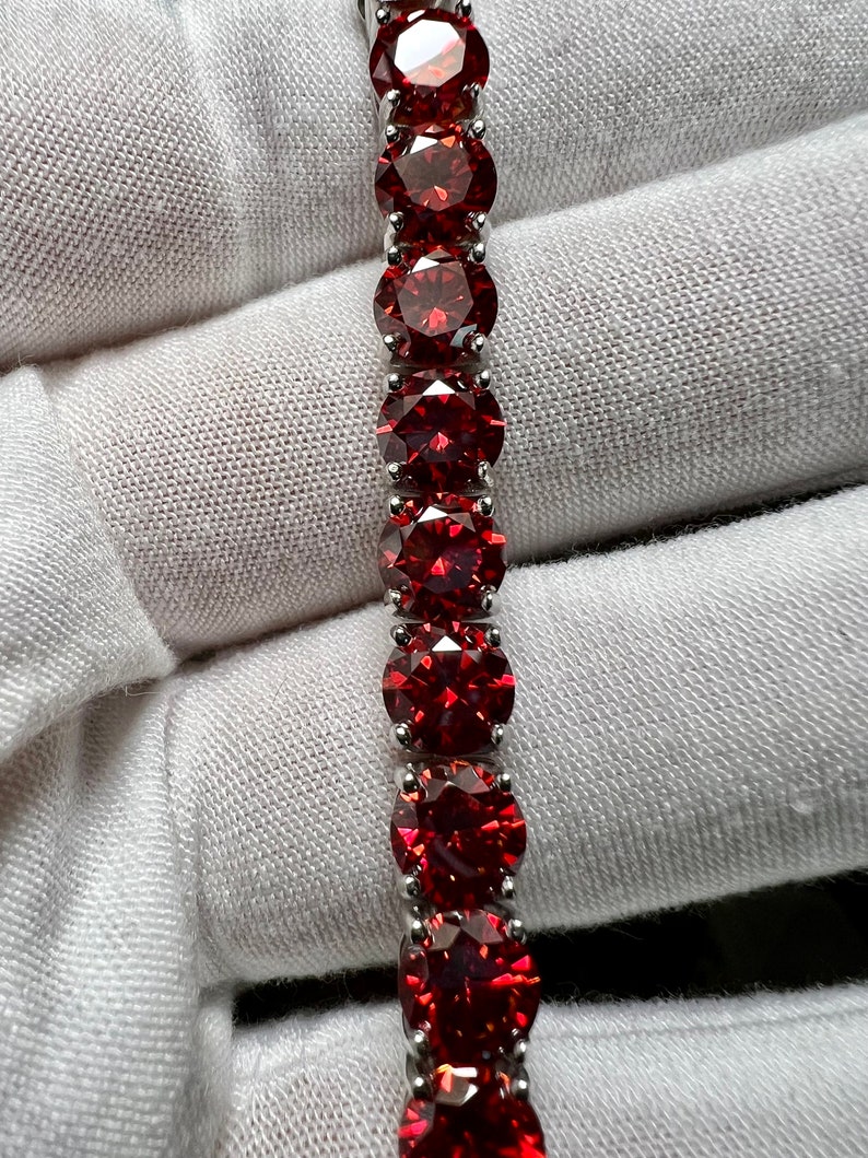 May include: A silver bracelet with a row of red round gemstones.
