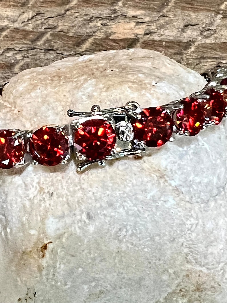 May include: A silver bracelet with a clasp and red round stones.