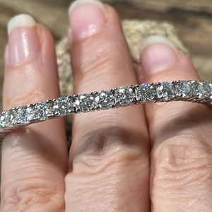 K&ouml;nnte beinhalten: Nahaufnahme eines Tennisarmbands mit einer Reihe funkelnder, rund geschliffener Diamanten, die in einem silbernen Band gefasst sind. Das Armband wird von einer Person gehalten. Die Diamanten reflektieren das Licht.