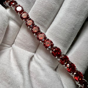 May include: A silver tennis bracelet with a row of red round gemstones.