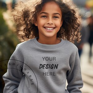 Può includere: Una giovane persona indossa una felpa grigia con la scritta "YOUR DESIGN HERE" stampata sul davanti. La felpa è una tela bianca per la personalizzazione.