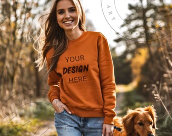 以下が含まれることがあります： 女性が、前面に「YOUR DESIGN HERE」という文字が印刷された焦げ茶色のスウェットシャツを着ています。彼女は犬と一緒に森の中に立っています。
