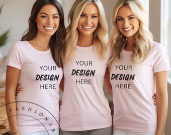 May include: Three women wearing pink t-shirts with the text "YOUR DESIGN HERE" printed on the front. The women are standing in front of a window.